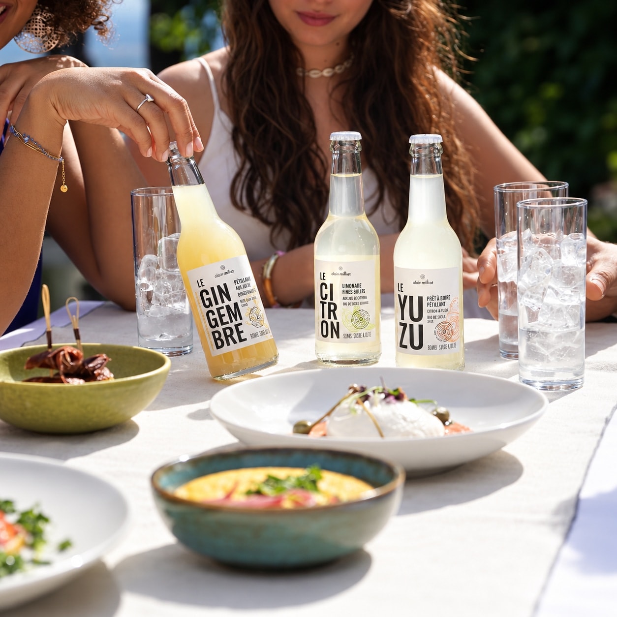 Bouteilles de jus Alain Milliat dégustées à table en terrasse, entourées de mets raffinés