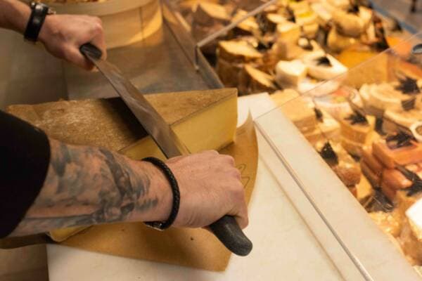 Le fromager tranche un morceau de pâte pressée au couteau derrière la vitrine