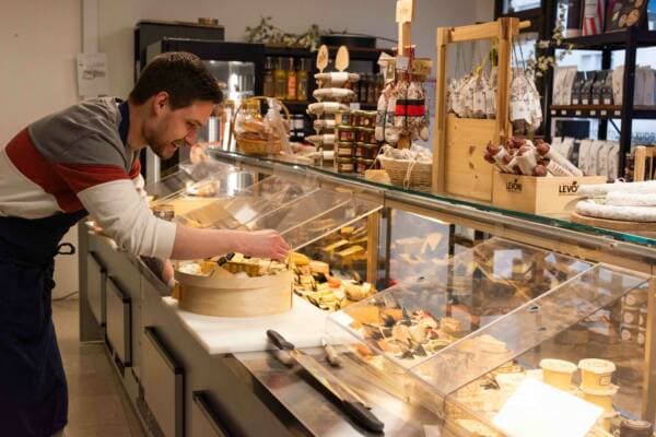 Un fromager compose un plateau dans une boîte en bois, penché sur la vitrine