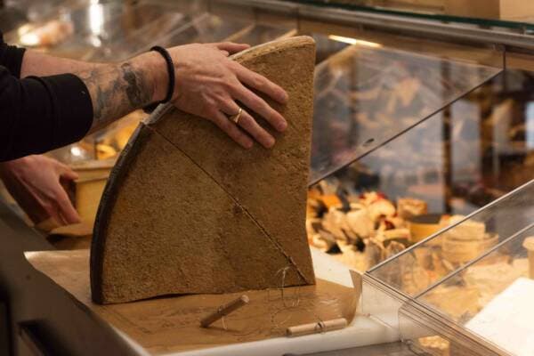 Un fromager coupe un quart de meule à la lyre sur le plan de travail