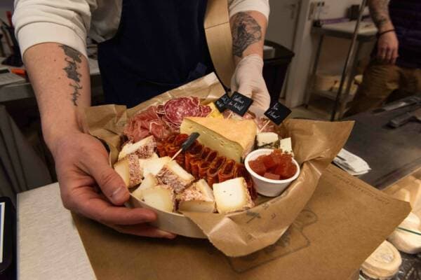 Un vendeur présente un plateau apéritif de charcuterie et de fromages dans sa barquette kraft