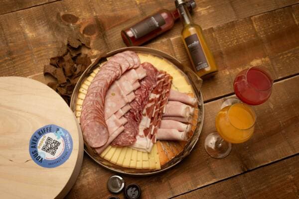 Plateau de charcuterie et de fromages vu de dessus, accompagné de deux jus de fruits